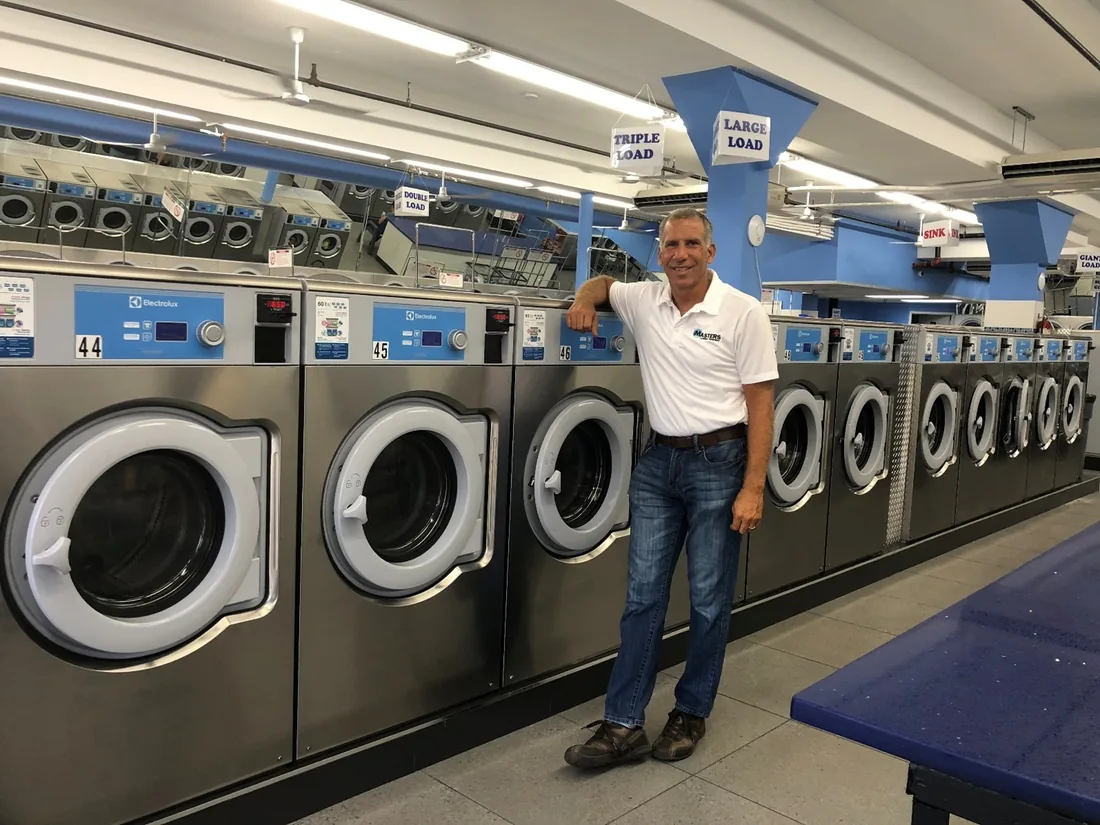 Michael Mastorides standing beside a row of newly installed Electrolux washers in a laundromat