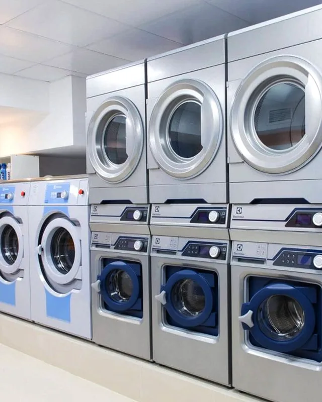 Stacked commercial washers and dryers installed along a laundromat wall