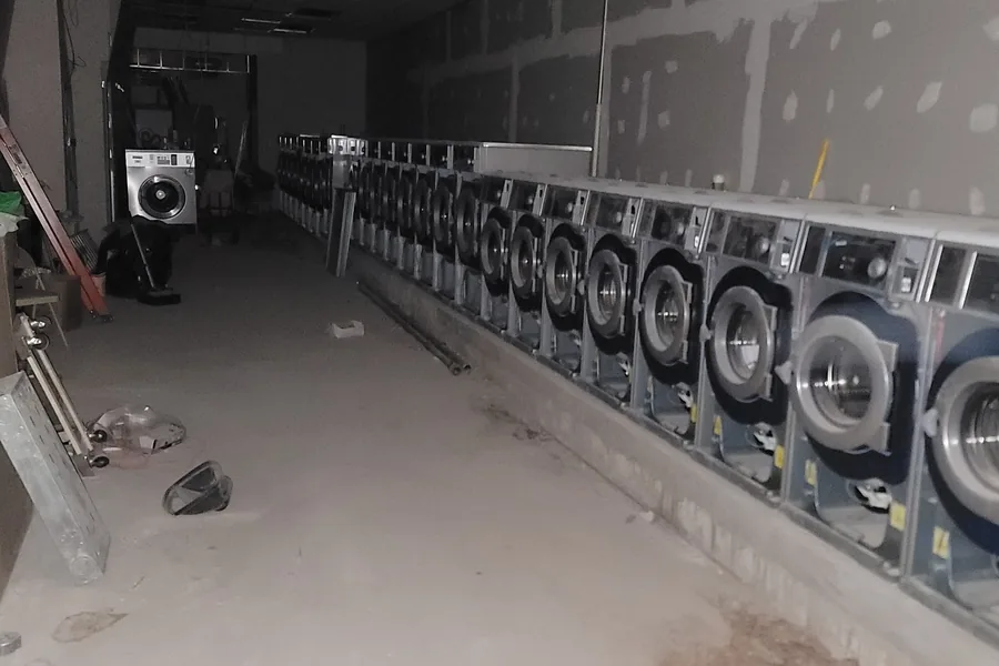 Long row of commercial washers installed along a wall in a laundromat still under construction
