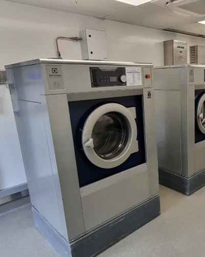 Electrolux on-premises washers installed in a tiled laundry room with stainless sinks alongside