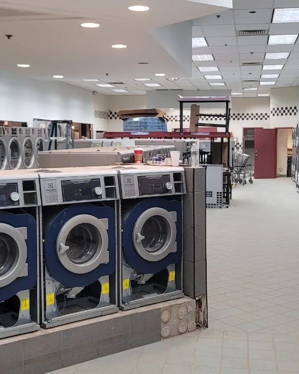 Commercial washers installed on a raised plinth in a laundromat, with the store's earlier machines still in place behind them